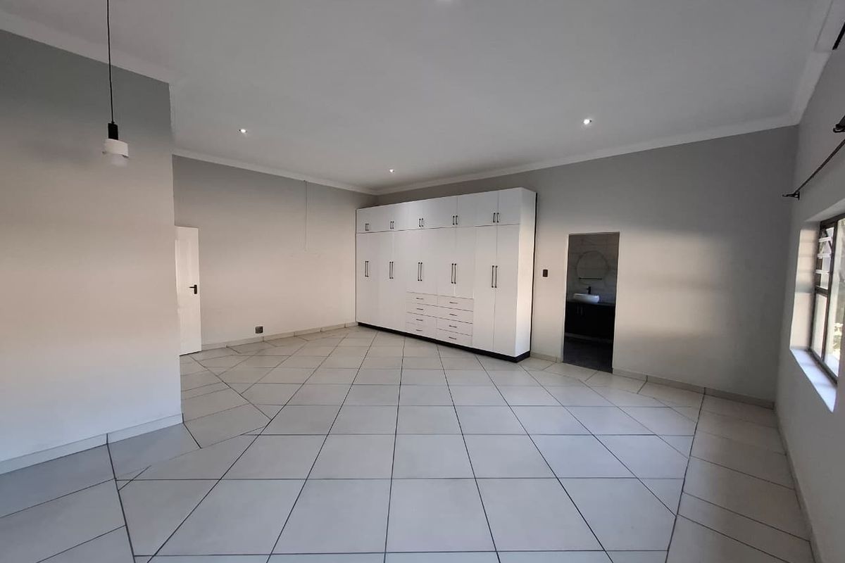 Spacious bedroom featuring large built-in cupboards, neutral tiled flooring, and modern recessed lighting, offering a clean and versatile living space.