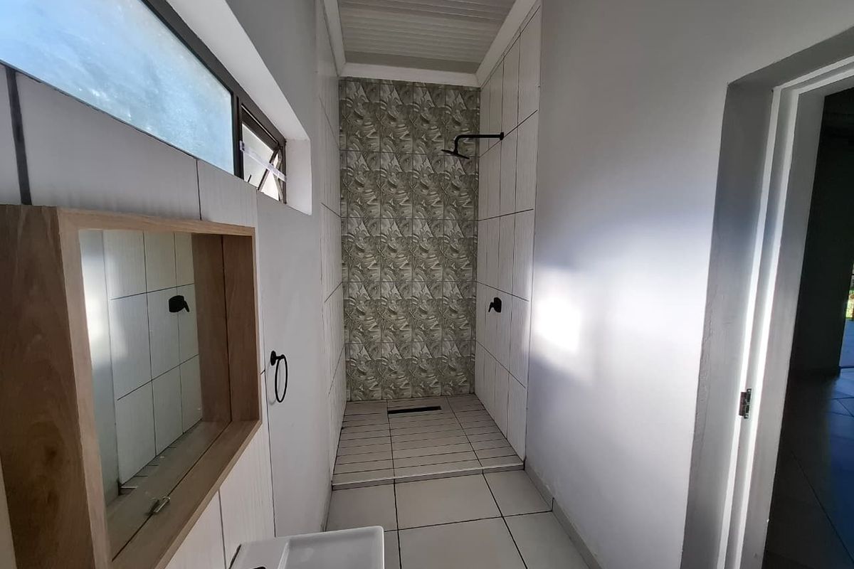 A modern, clean bathroom featuring a walk-in shower with patterned tile accents, a wall-mounted mirror, and a minimalist basin.