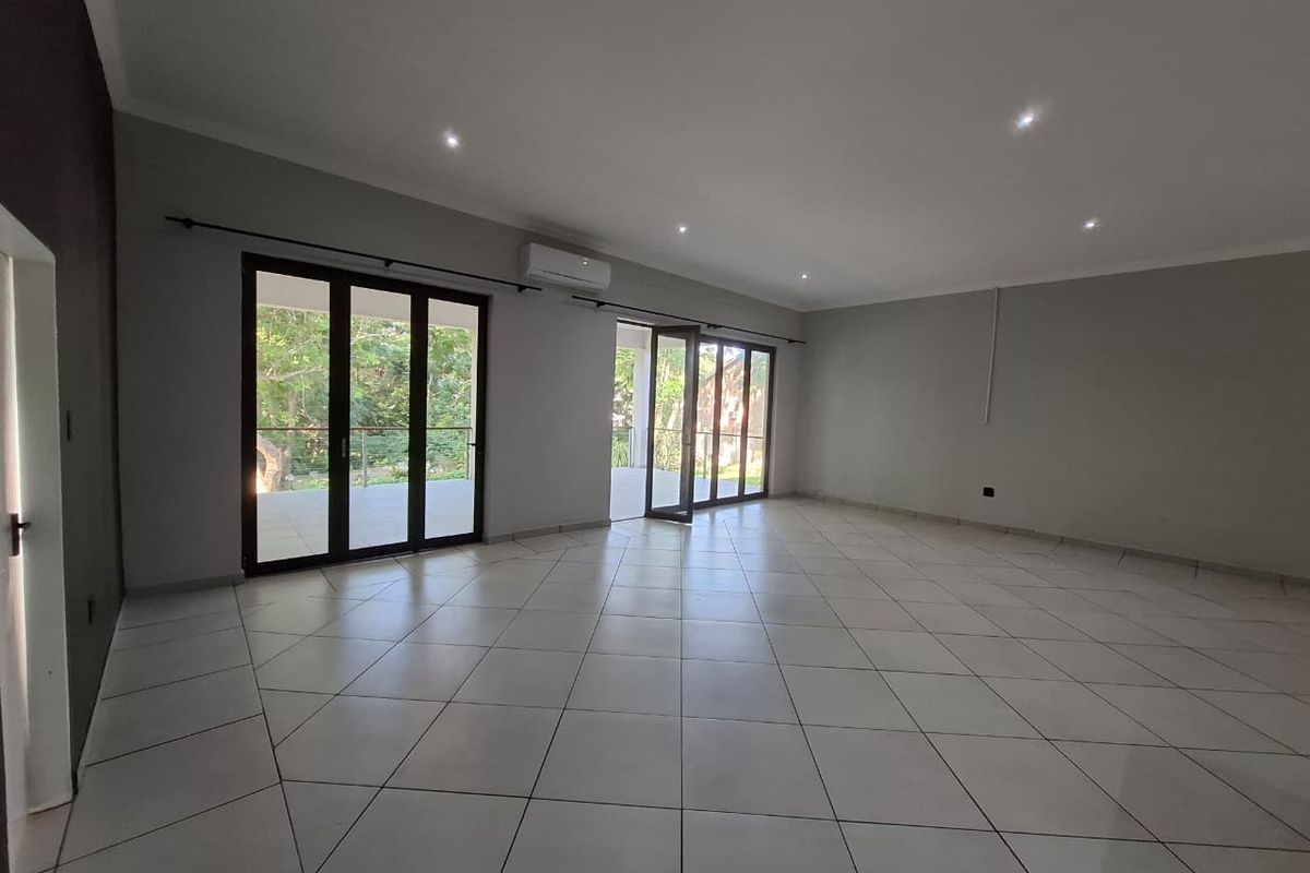 Spacious, light-filled living area featuring neutral tiled flooring, recessed downlighting, and large aluminium sliding doors providing seamless access to the outdoor patio.