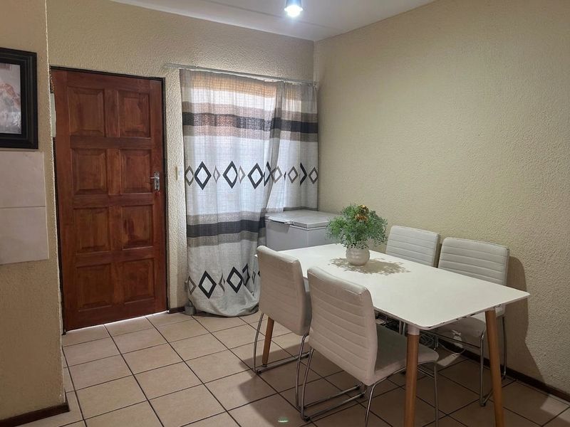 A functional dining area featuring tiled flooring, textured walls, and a solid wood entrance door.