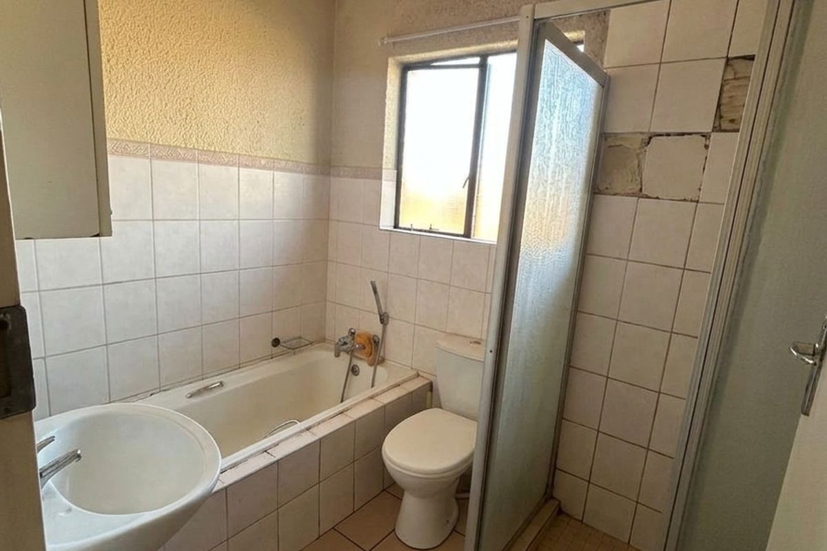 A dated bathroom featuring a pedestal basin, bathtub, toilet, and shower enclosure, currently requiring significant cosmetic repairs and retiling.