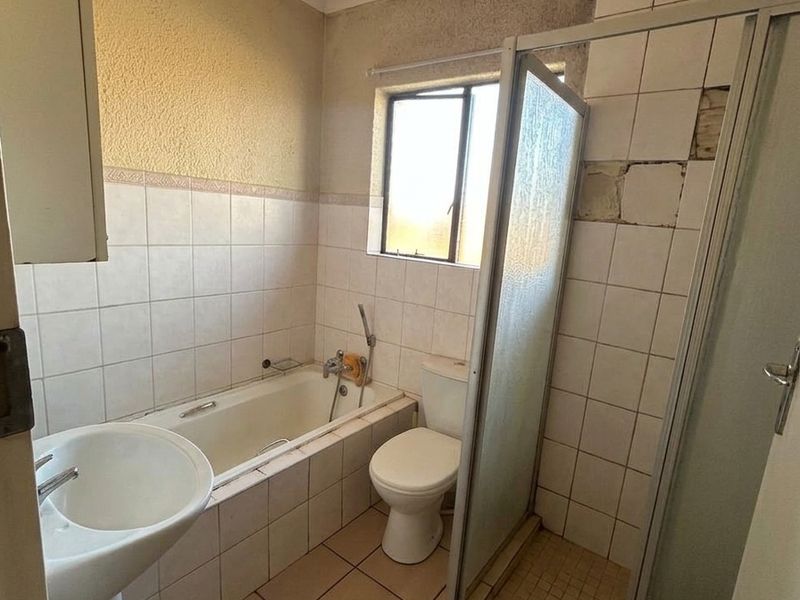 A dated bathroom featuring a pedestal basin, bathtub, toilet, and shower enclosure, currently requiring significant cosmetic repairs and retiling.