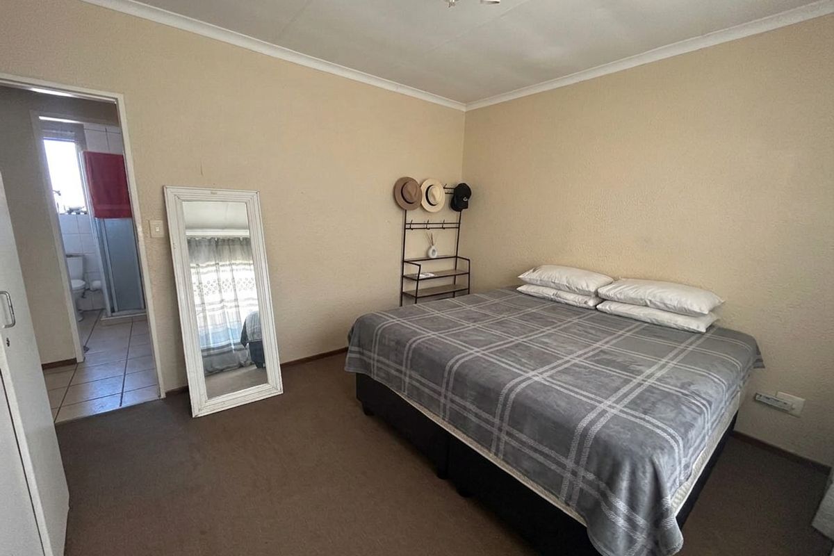 A standard bedroom featuring carpeted flooring, cove cornicing, and an en-suite bathroom access point.