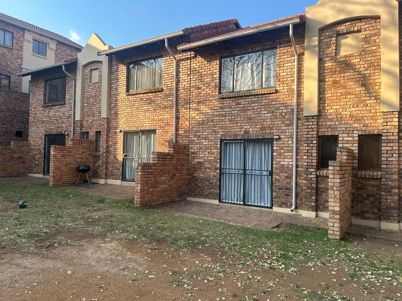 Rear view of a face brick townhouse featuring paved patio areas, sliding glass doors with security gates, and a shared garden space.