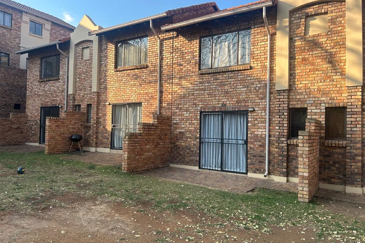 Rear view of a face brick townhouse featuring paved patio areas, sliding glass doors with security gates, and a shared garden space.