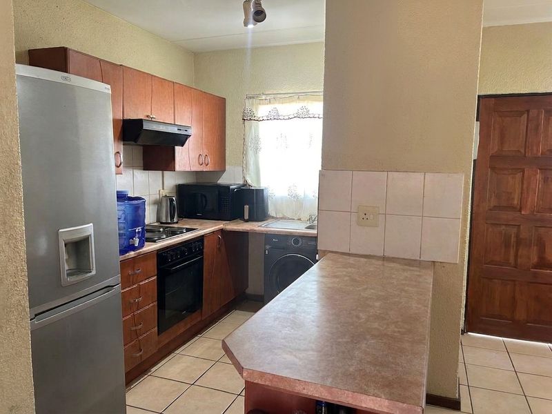 A functional kitchen featuring wood-finish cabinetry, laminate countertops, a breakfast bar, and tiled flooring, offering a practical layout for daily meal preparation.