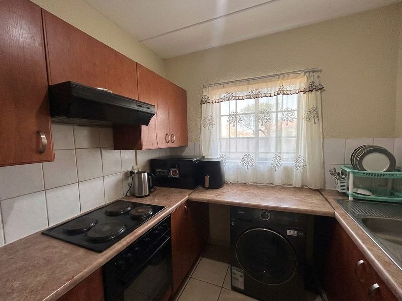 Compact kitchen featuring laminate countertops, built-in cabinetry, an electric hob with extractor fan, and tiled flooring with space for laundry appliances.