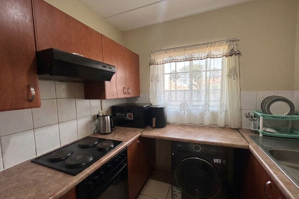 Compact kitchen featuring laminate countertops, built-in cabinetry, an electric hob with extractor fan, and tiled flooring with space for laundry appliances.