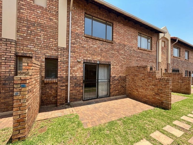 Rear view of a face brick townhouse featuring a private paved patio area, sliding glass door with security gate, and a small lawn.