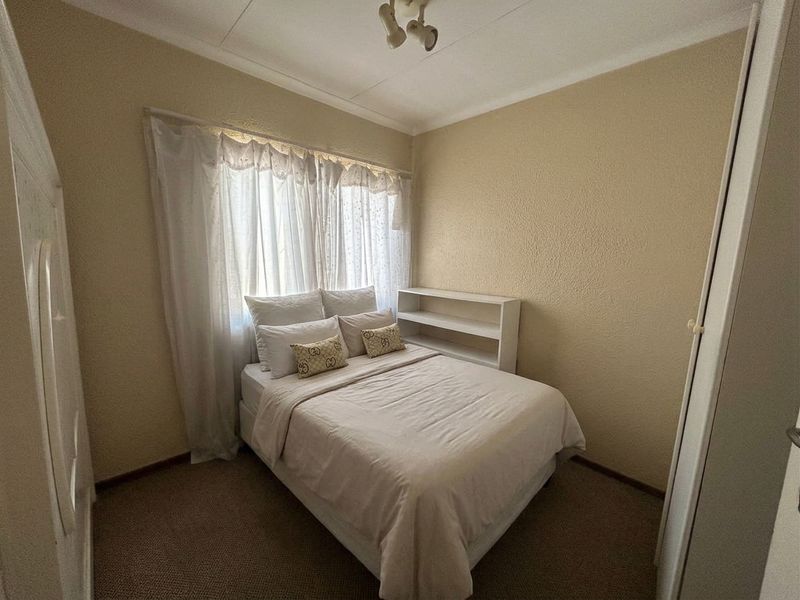 A compact bedroom featuring neutral wall finishes, carpeted flooring, and a built-in wardrobe, providing a functional and simple living space.
