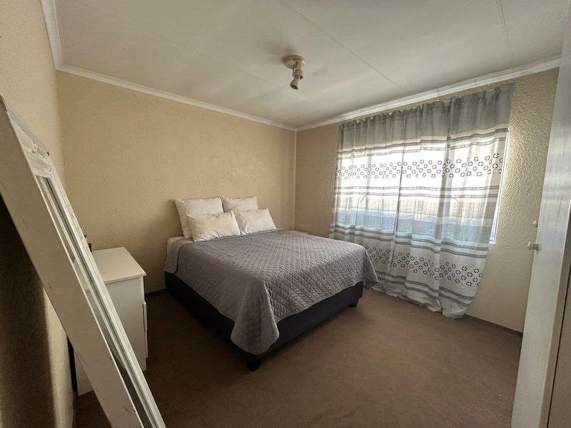 A standard bedroom featuring carpeted flooring, neutral wall finishes, and a window with installed curtain rails.