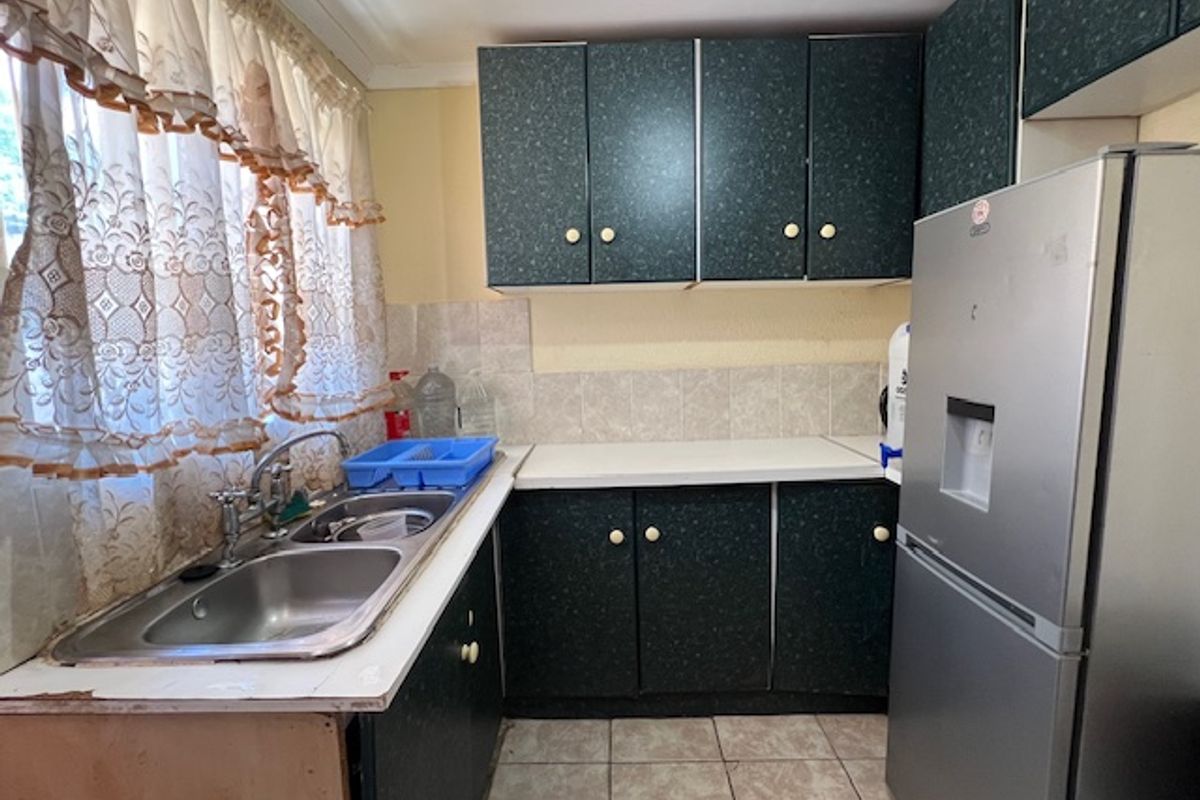 A dated kitchen featuring dark laminate cabinetry, a double bowl stainless steel sink, tiled splashback, and tiled flooring.