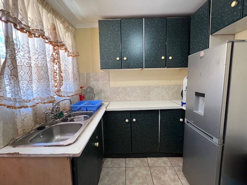 A dated kitchen featuring dark laminate cabinetry, a double bowl stainless steel sink, tiled splashback, and tiled flooring.