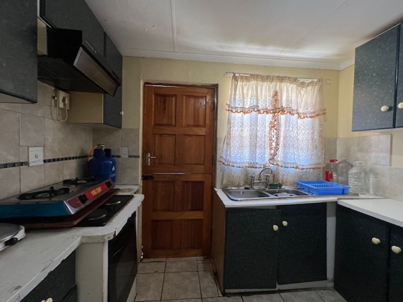 A dated kitchen featuring built-in cabinetry, a double sink, tiled splashbacks, and a solid wood exterior door, offering potential for modernization.