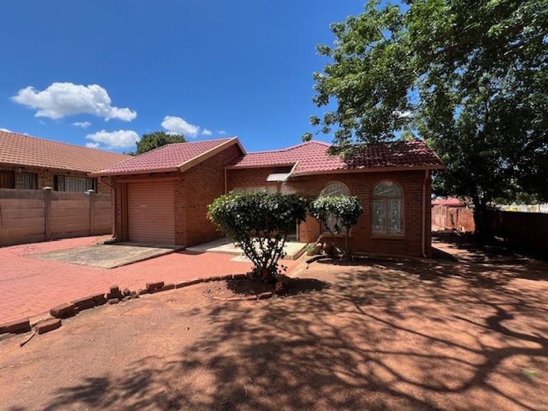 Front view of a face brick house featuring a tiled roof, single garage, and paved driveway area.