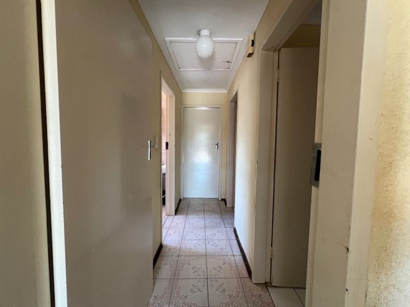 A functional hallway featuring ceramic floor tiles and access to multiple rooms, requiring cosmetic updates to improve its overall appearance.