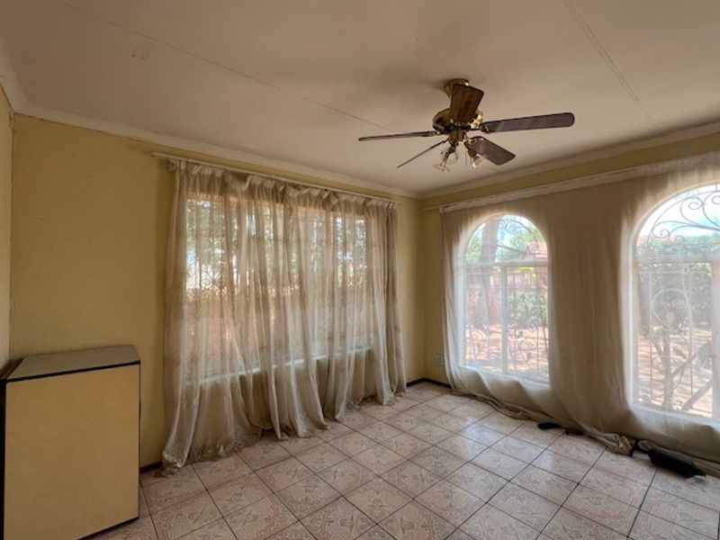 A vacant living room featuring tiled flooring, a ceiling fan, and arched windows with security bars, offering a blank canvas for renovation.