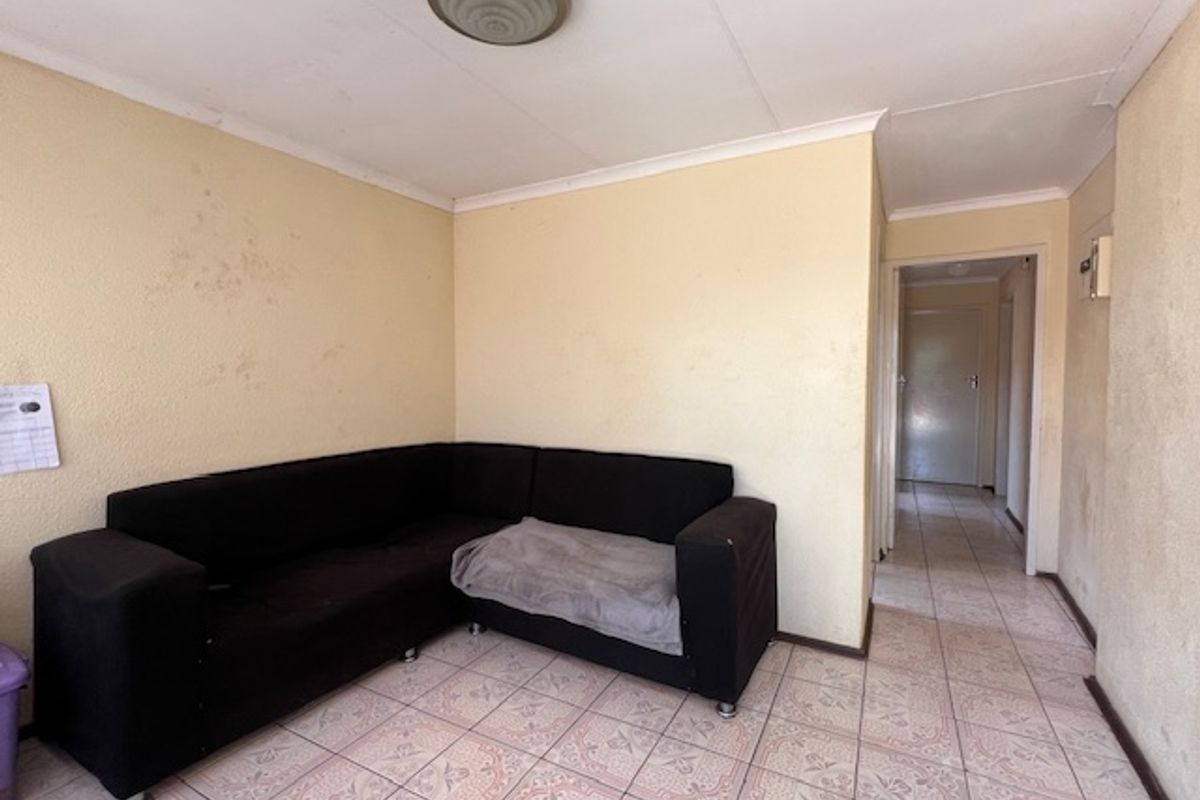 A living room area featuring tiled flooring and coved ceilings, requiring cosmetic updates to the wall finishes.