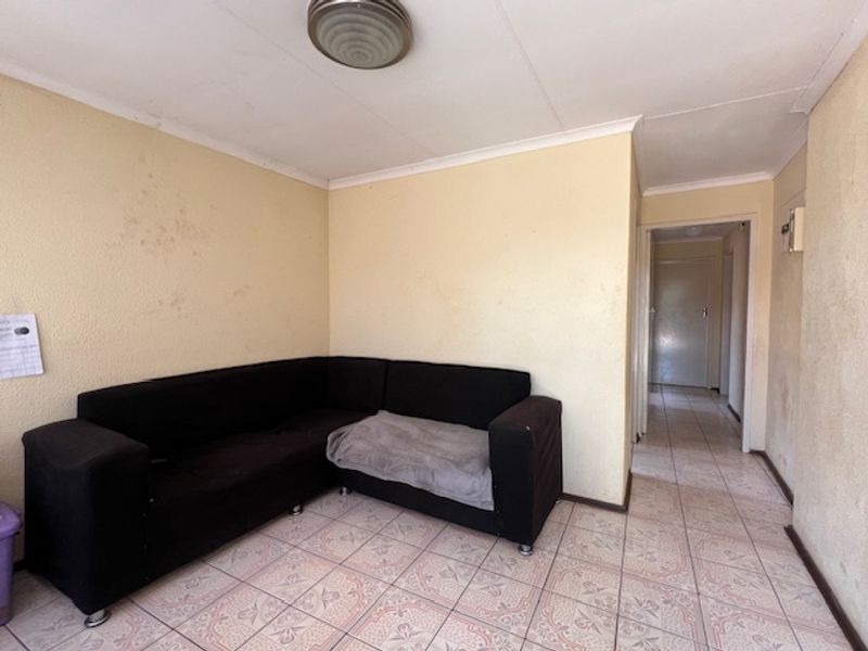 A living room area featuring tiled flooring and coved ceilings, requiring cosmetic updates to the wall finishes.