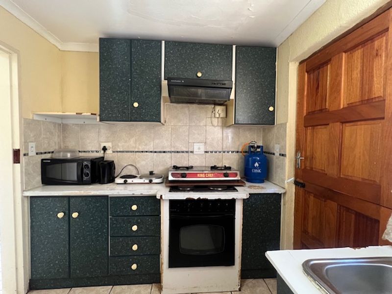 Compact kitchen featuring dark laminate cabinetry, tiled backsplash, built-in oven with gas hob, and a solid timber door.
