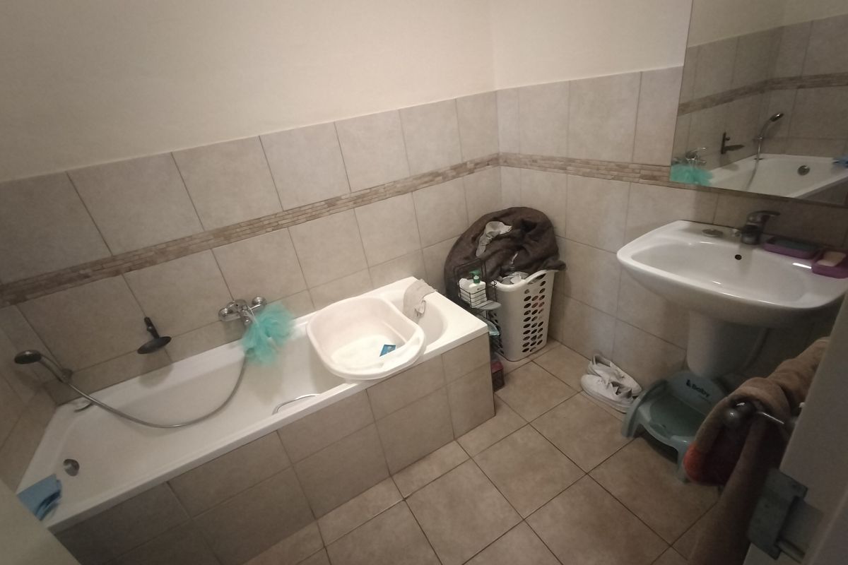 A functional bathroom featuring a bathtub with shower mixer, pedestal basin, and neutral wall tiling.