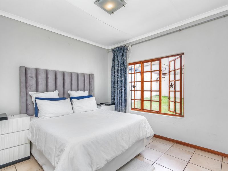 A bedroom featuring tiled flooring, wooden window frames with security bars, and a central ceiling light fixture.