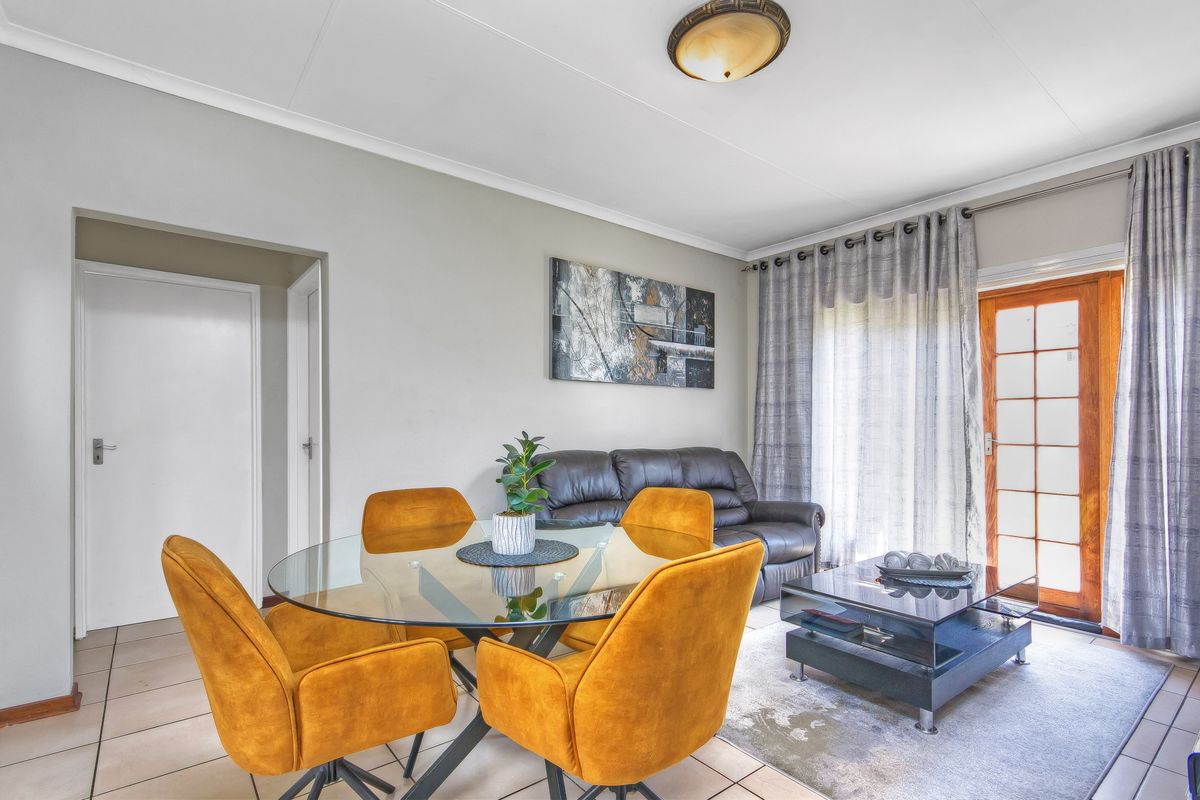 A bright living and dining area featuring tiled flooring, coved ceilings, and a timber-framed glass door providing access to the exterior.