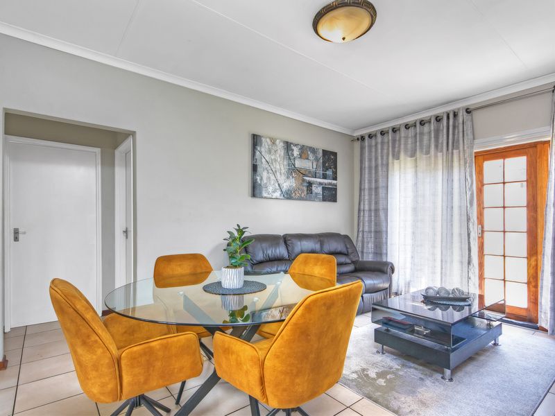 A bright living and dining area featuring tiled flooring, coved ceilings, and a timber-framed glass door providing access to the exterior.