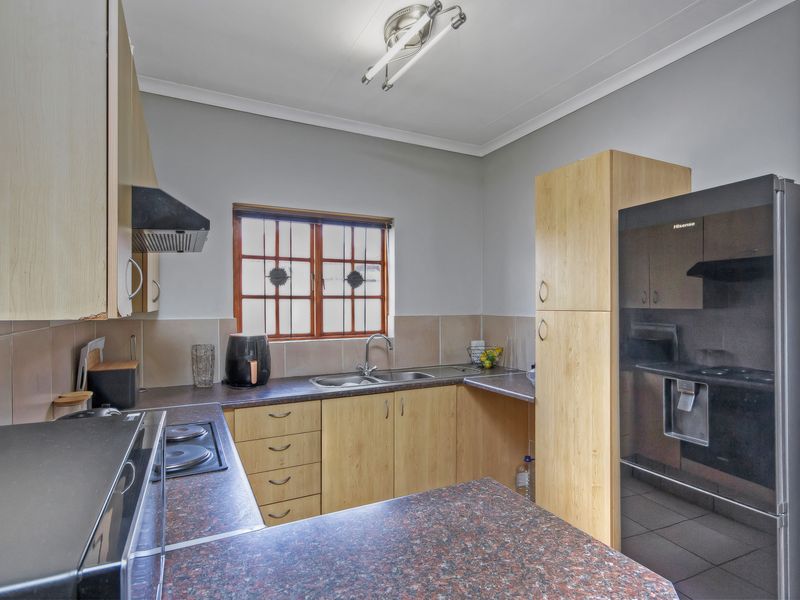 Functional kitchen featuring laminate cabinetry, dark countertops, built-in hob with extractor fan, and a tiled splashback with a window overlooking the exterior.