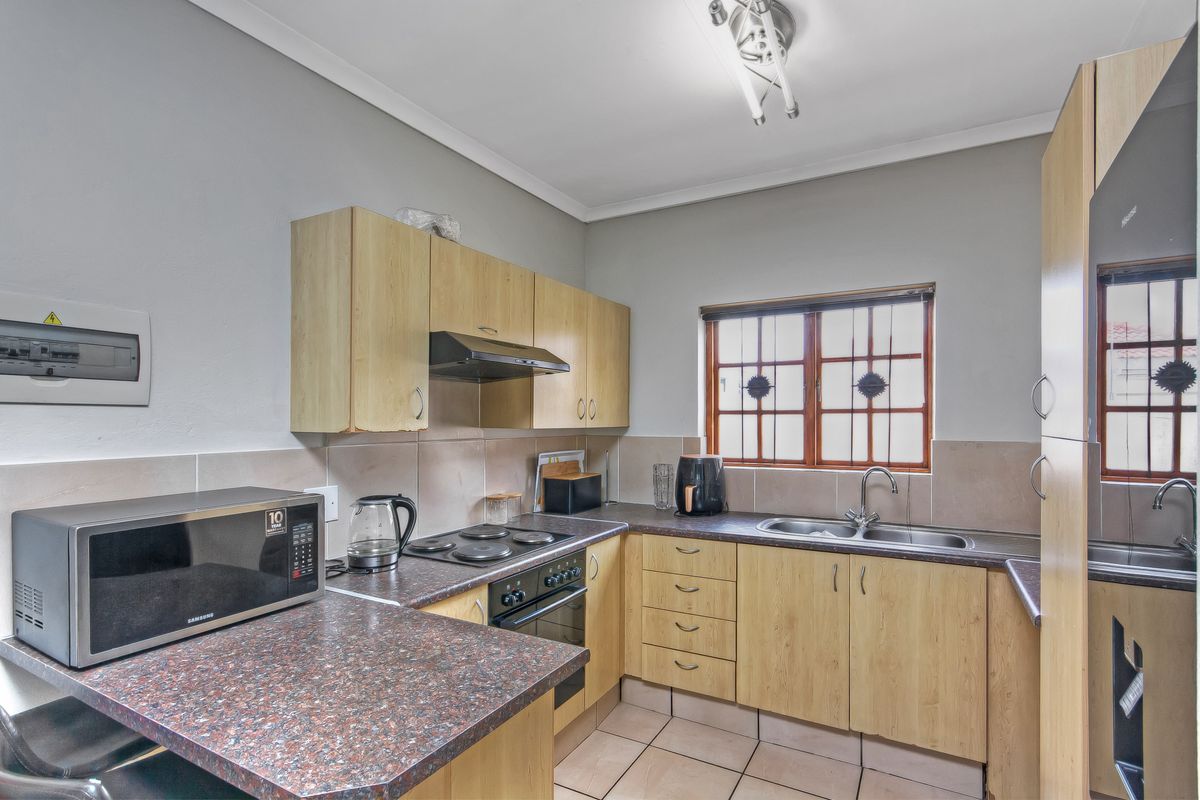 Functional kitchen featuring laminate cabinetry, dark countertops, built-in oven with hob, extractor fan, and a stainless steel double sink.