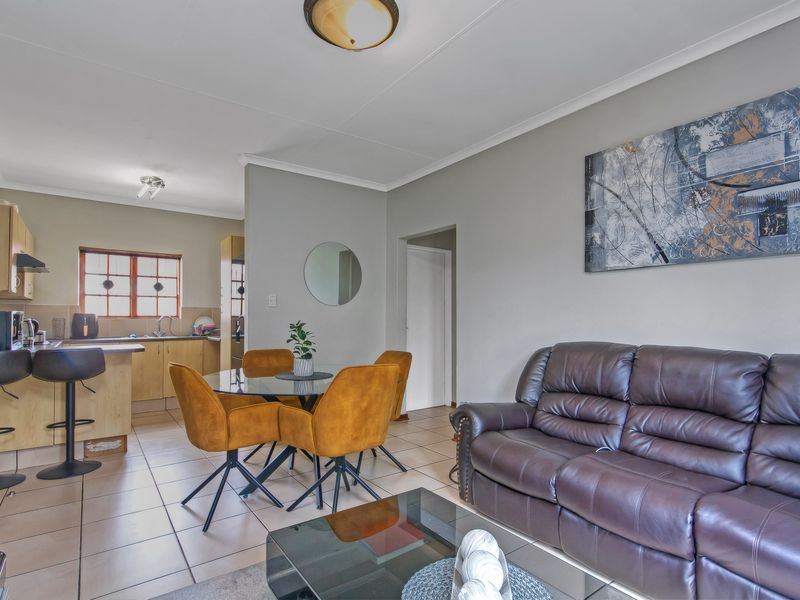 Open-plan living and kitchen area featuring tiled flooring, neutral wall tones, and functional built-in cabinetry with a breakfast bar.