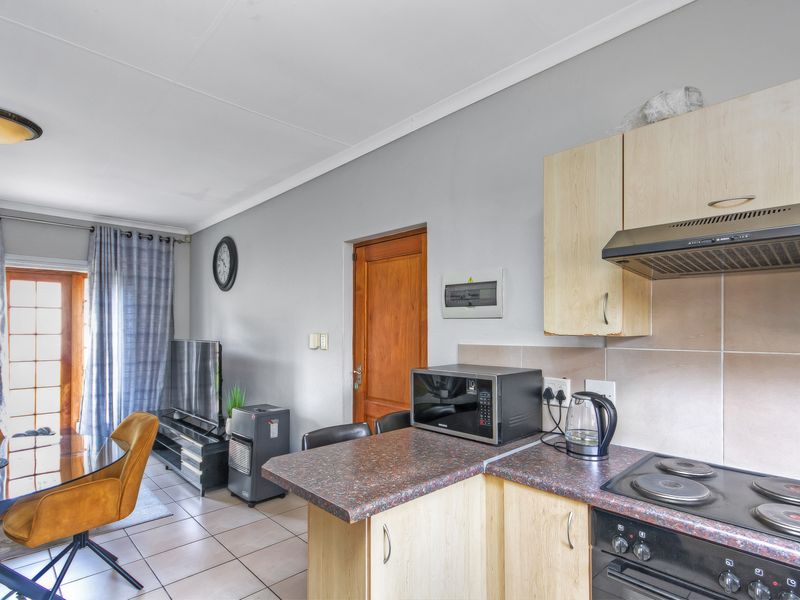 Open-plan living and kitchen area featuring tiled flooring, light wood-finish cabinetry, and integrated cooking appliances, providing a functional and connected living space.