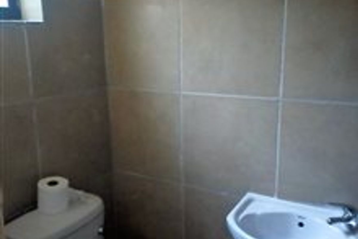 A compact bathroom featuring tiled walls, a pedestal basin, and a standard toilet.