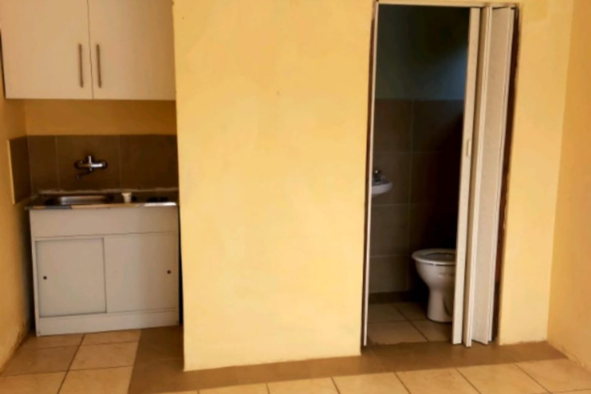 A compact kitchen area featuring basic cabinetry and a sink, with an adjacent small bathroom accessible via a folding door.