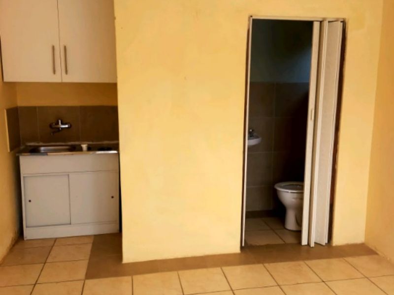 A compact kitchen area featuring basic cabinetry and a sink, with an adjacent small bathroom accessible via a folding door.