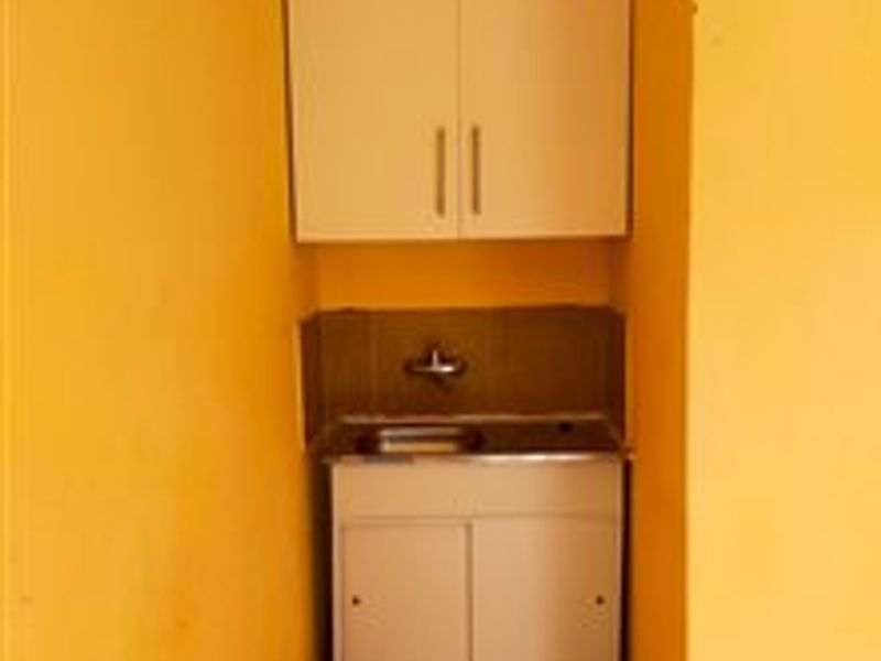 A compact scullery or utility area featuring built-in cabinetry, a stainless steel sink, and a tiled backsplash.