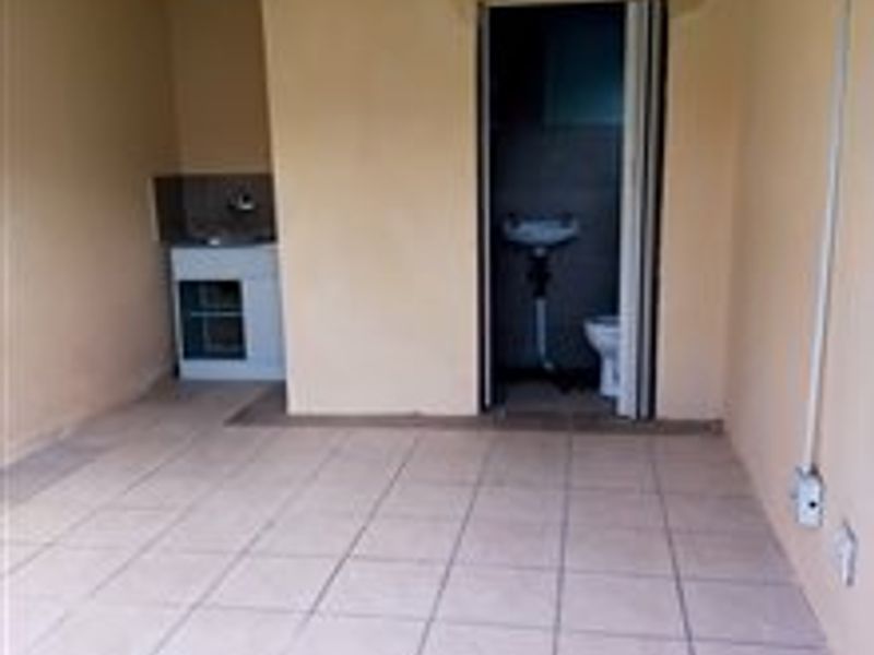 An empty open-plan studio space featuring tiled flooring, a small kitchenette area, and an adjoining bathroom with basic fixtures.
