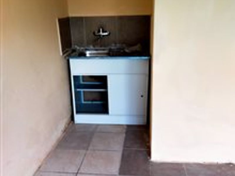 A compact scullery or utility area featuring a built-in sink, base cabinetry, and tiled flooring, suitable for laundry or secondary kitchen prep.