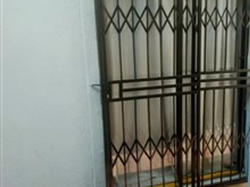 A small outdoor patio area featuring a metal security gate and sliding door access.