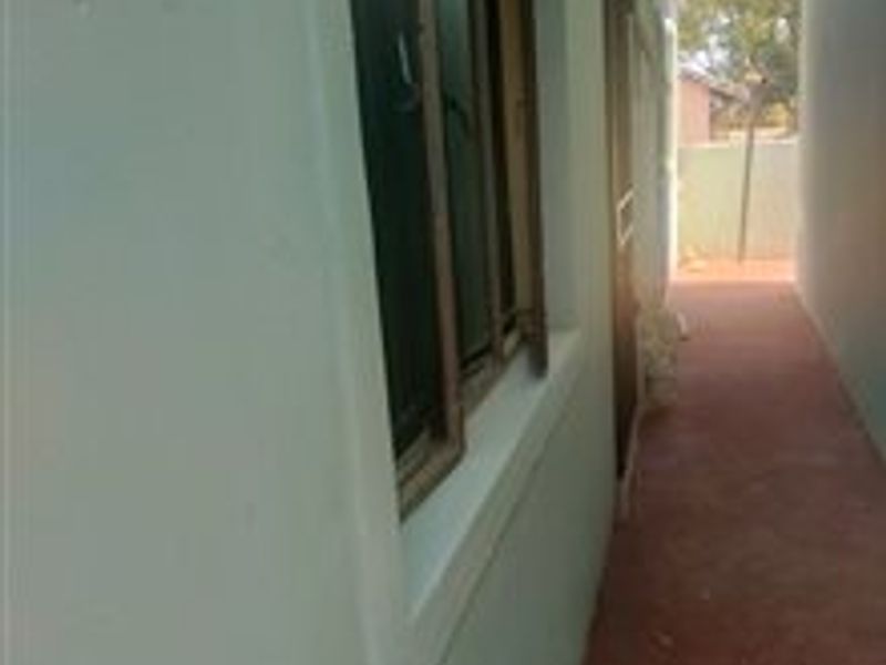 A narrow exterior side passage featuring a paved walkway and timber-framed windows along the building facade.
