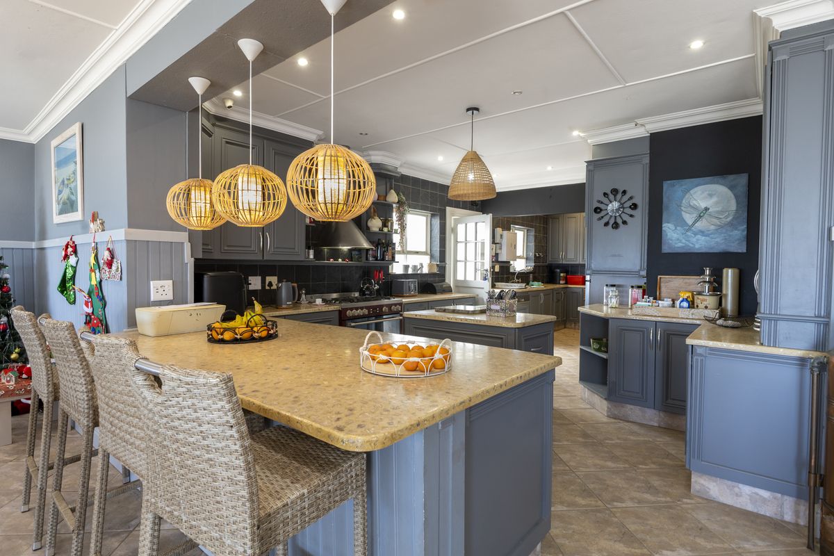 Spacious kitchen featuring a large central island with stone countertops, shaker-style cabinetry, tiled backsplash, and modern pendant lighting.