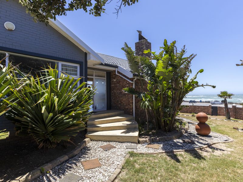 Front entrance of a brick-clad house featuring concrete steps, a chimney, and a landscaped garden with ocean views in the background.