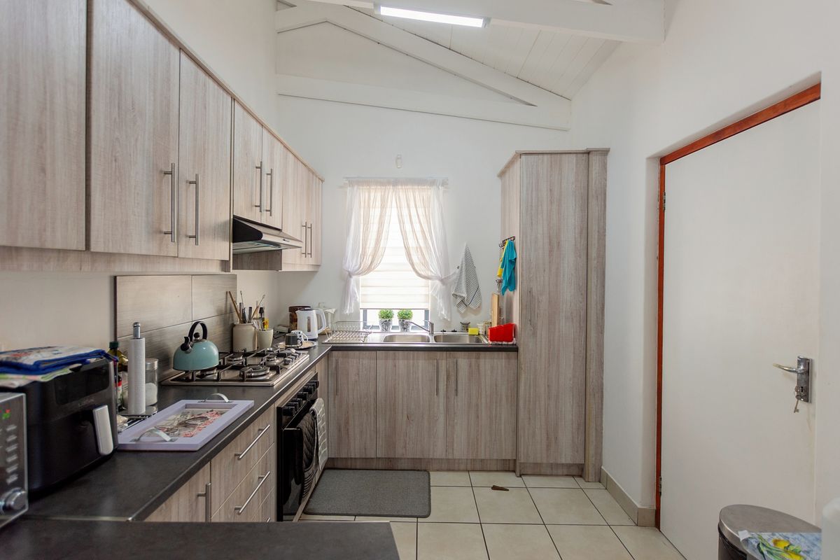 A functional kitchen featuring light wood-grain cabinetry, a gas hob with extractor, built-in oven, double sink, and vaulted ceilings with tiled flooring.