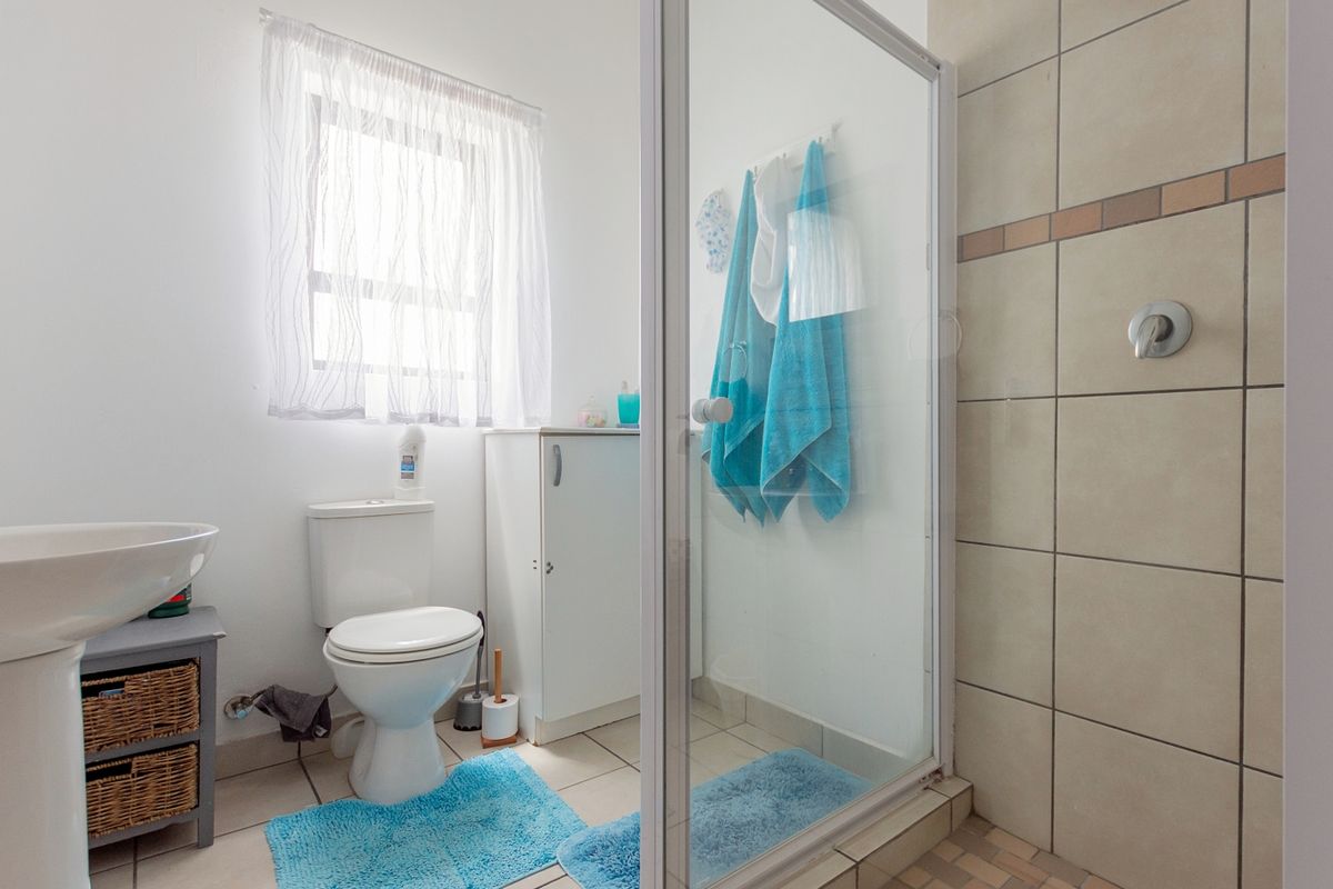 A functional bathroom featuring a pedestal basin, toilet, and a glass-enclosed shower with neutral wall tiling and tiled flooring.