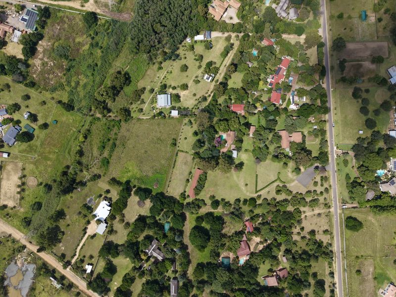 An aerial view of a residential area featuring multiple plots, established trees, and access roads within a semi-rural landscape.