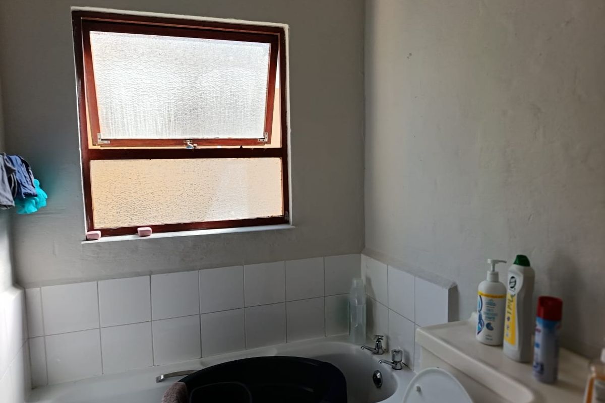 A functional bathroom featuring a standard bathtub with tiled splashback and a top-hung window, requiring cosmetic updates to improve its overall condition.