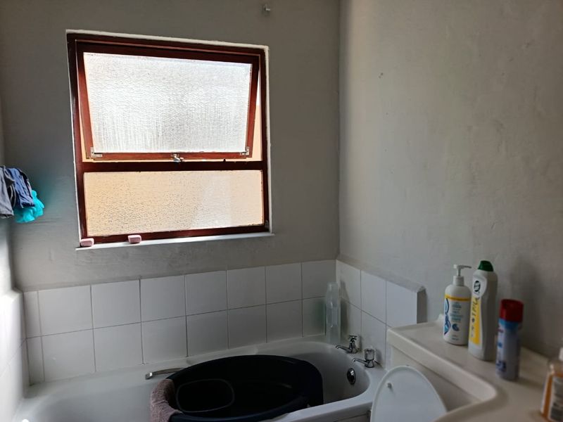A functional bathroom featuring a standard bathtub with tiled splashback and a top-hung window, requiring cosmetic updates to improve its overall condition.