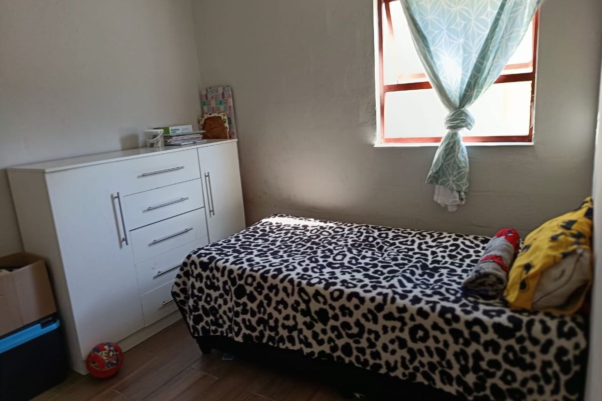 A compact bedroom featuring tiled flooring and a single window, providing a functional space with neutral wall finishes.