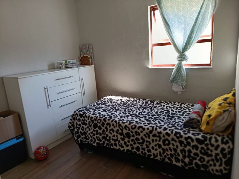 A compact bedroom featuring tiled flooring and a single window, providing a functional space with neutral wall finishes.