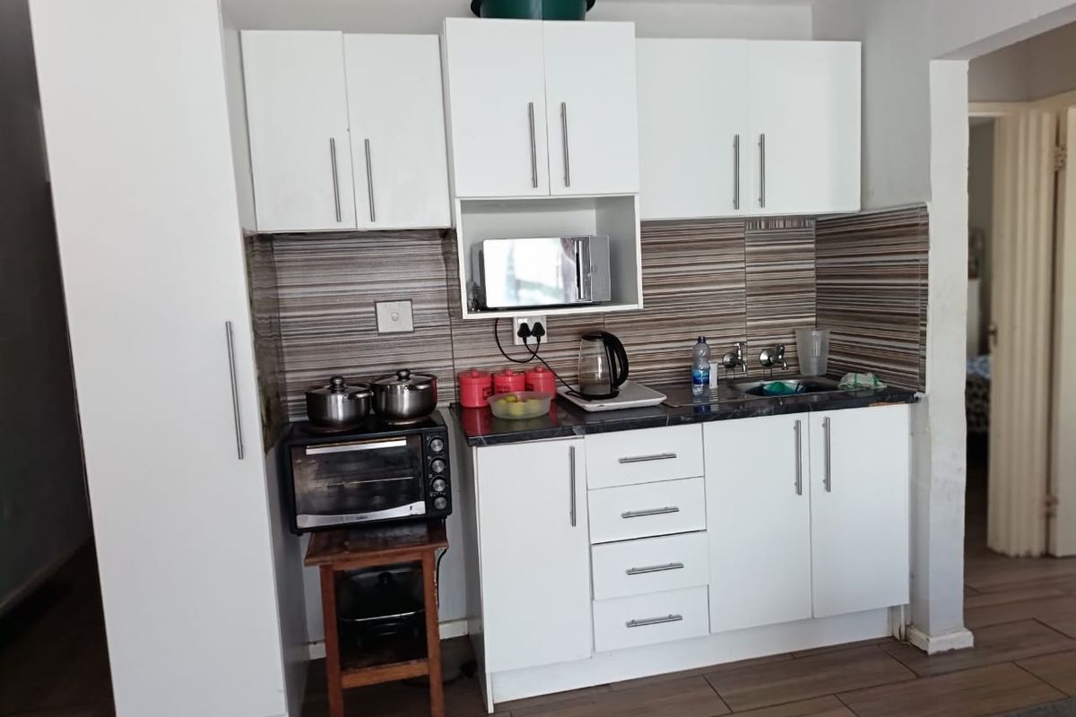 Compact kitchen featuring white cabinetry, a tiled backsplash, laminate countertops, and a stainless steel sink, with wood-look tiled flooring.